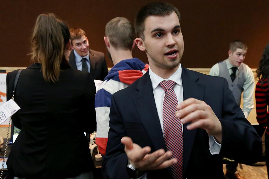 A student wearing a suit and tie gestures with his hands.