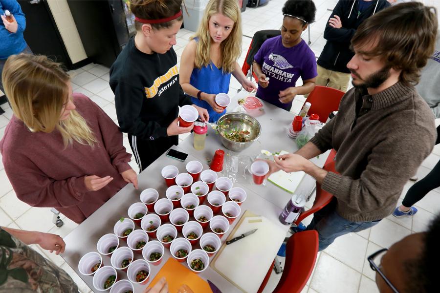 People gather around a table with red plastic cups filled with chopped food.