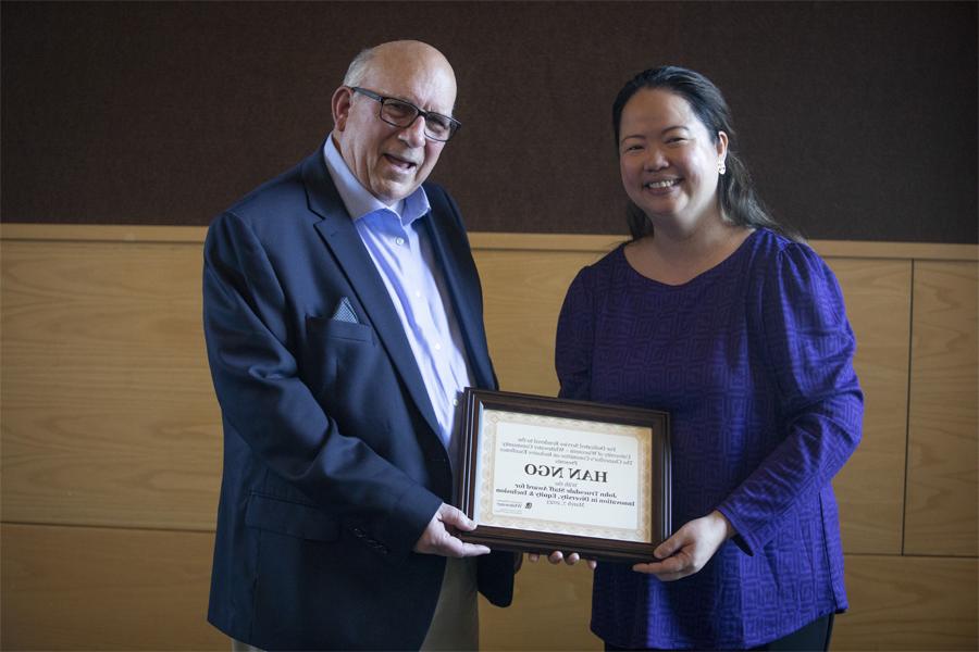 Two people stand together and hold a framed award.