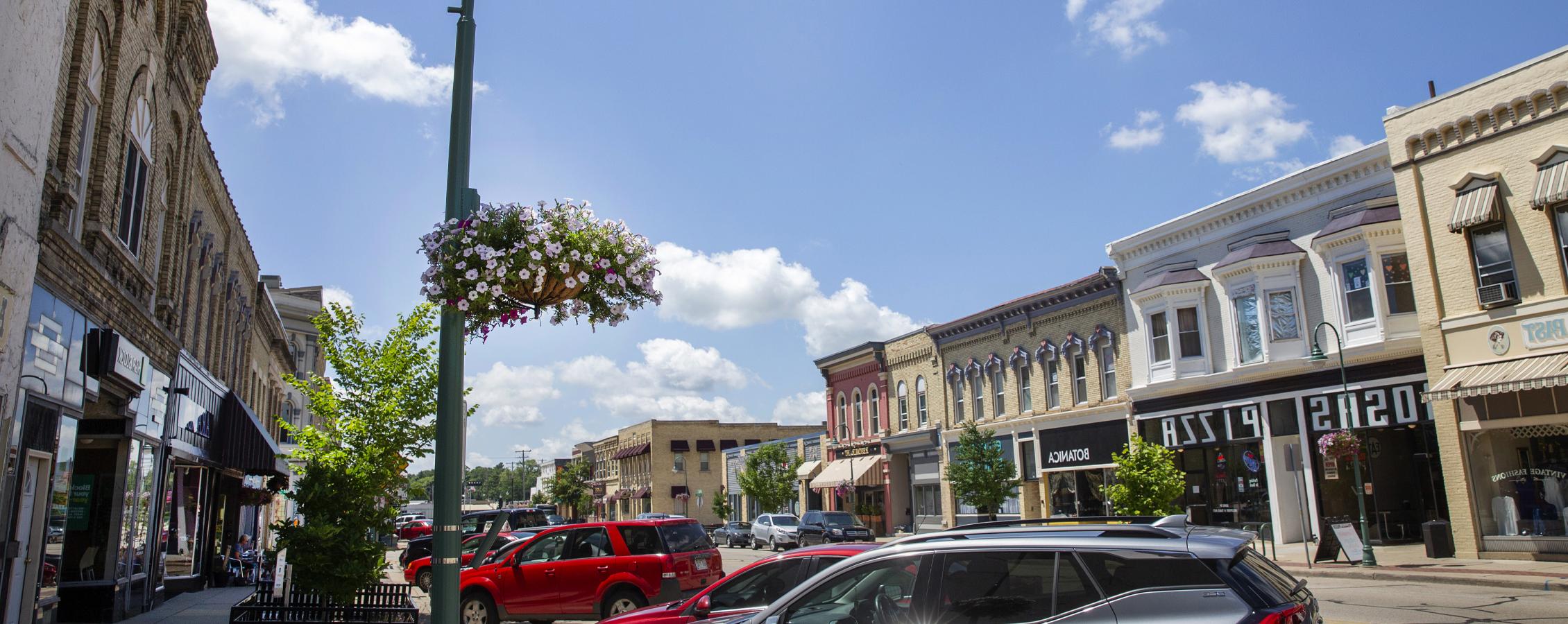 Buildings line the street in Downtown Whitewater with colorful flower pots hanging on the light posts.