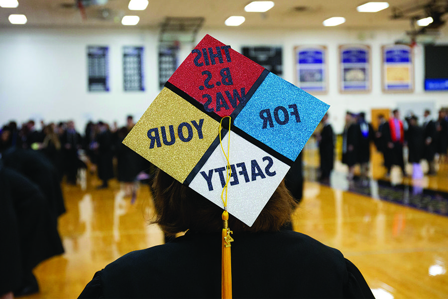 Student at graduation with text that reads "This B.S. was for your safety" printed on the back of their cap.